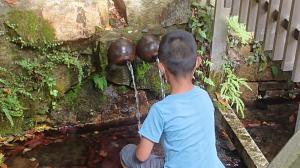 泉（御神体）から水をいただく児童の画像