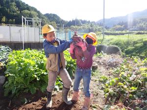 二人で協力し持ち上げられた大きな芋の画像