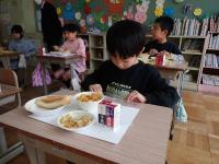コッペパンメニューの給食を食べる児童らの画像