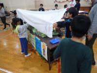 なかよし班で布を覆う作業をする児童らの画像
